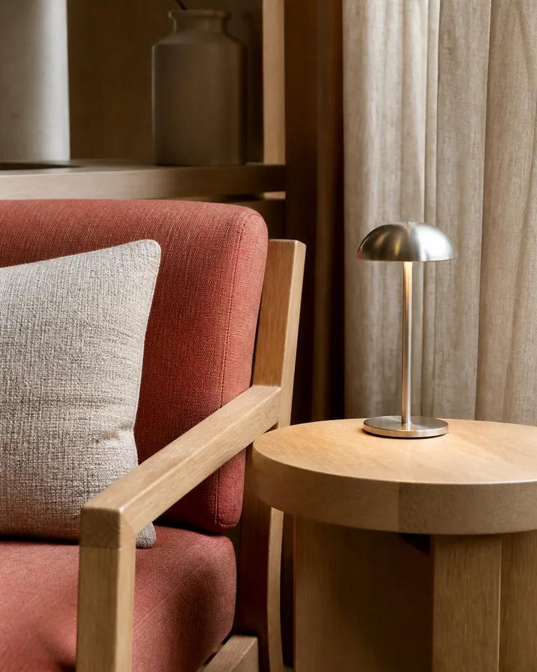 Detail van een loungefauteuil in koraalkleurig textiel naast een houten leestafel