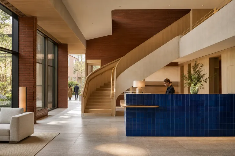 Lichte hotellobby met sculpturale trap, blauwe receptietegels en houten meubels