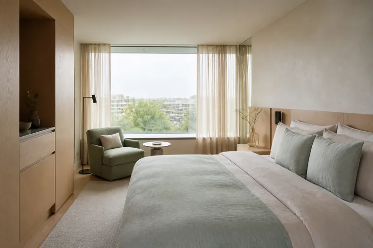 Lichte hotelkamer met linnen bed, zachtgroene fauteuil en breed raam
